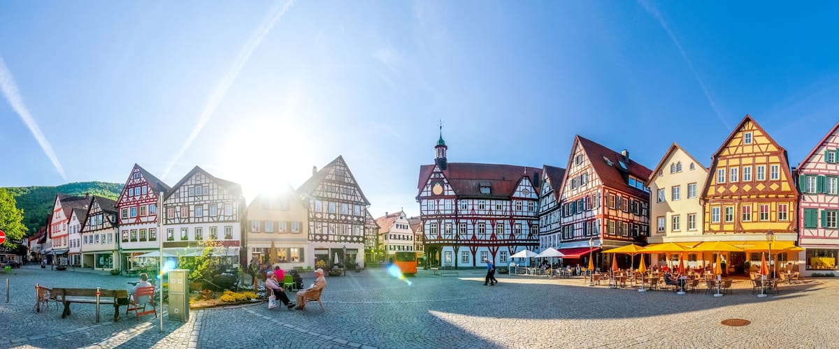 A cobblestone square with traditional half-timbered buildings, a tram, and outdoor seating areas.