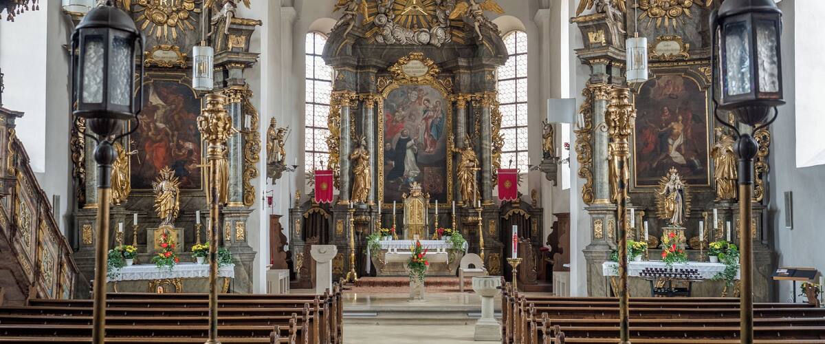 An ornate church interior with a crucifix, golden statues, and a large altar.