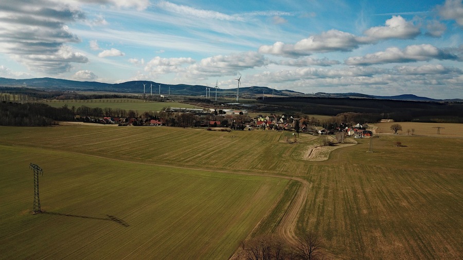 A rural landscape with wind turbines, fields, and a small village.