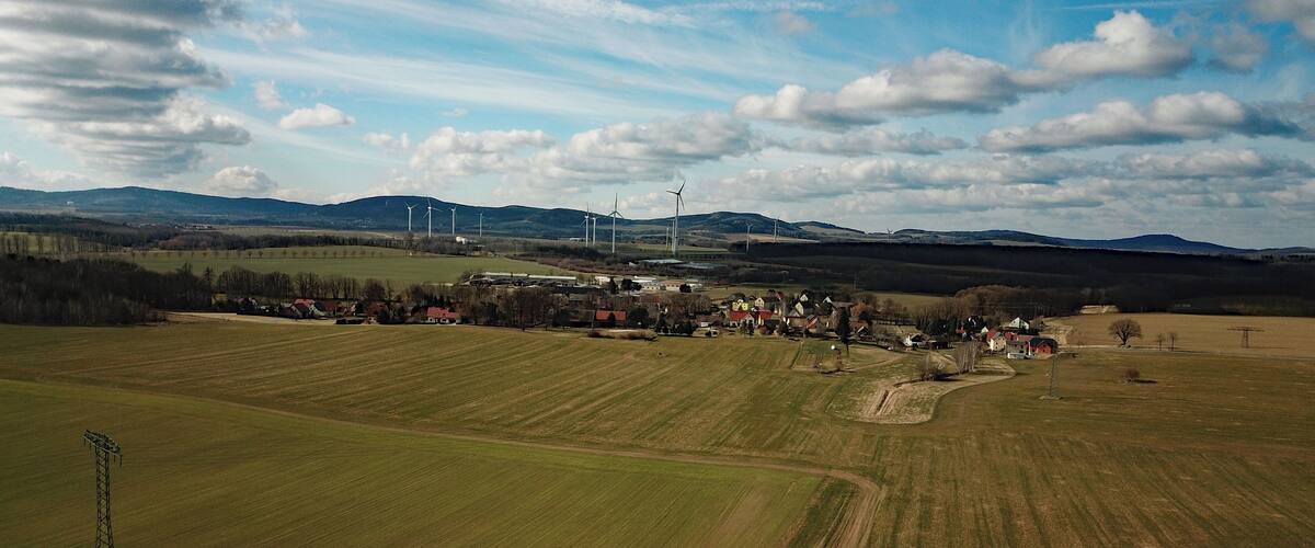 A rural landscape with wind turbines, fields, and a small village.
