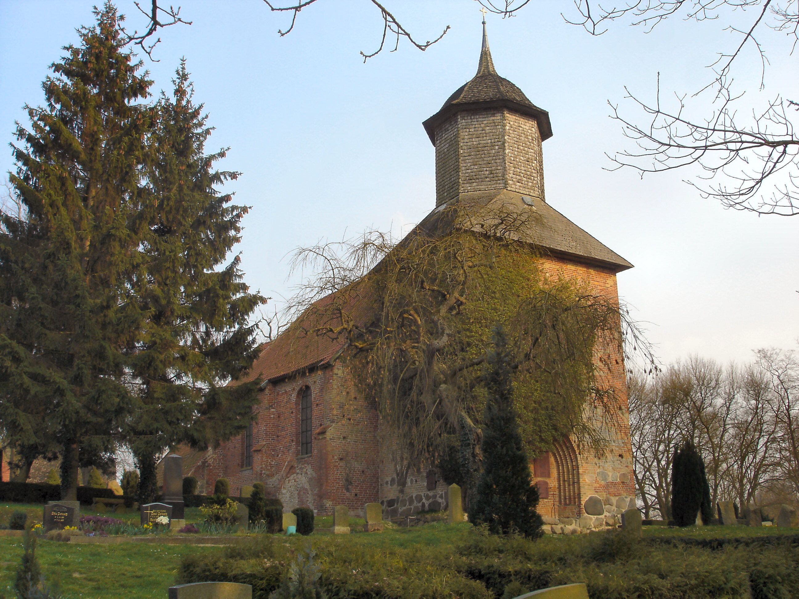 A church with a stone tower and ivy-covered walls, surrounded by a cemetery with headstones.