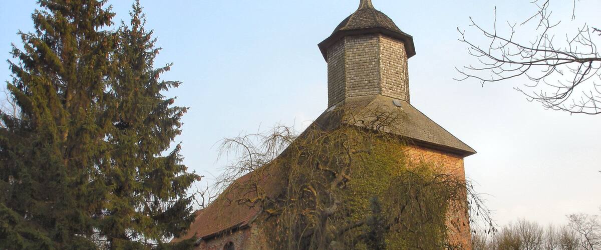 A church with a stone tower and ivy-covered walls, surrounded by a cemetery with headstones.