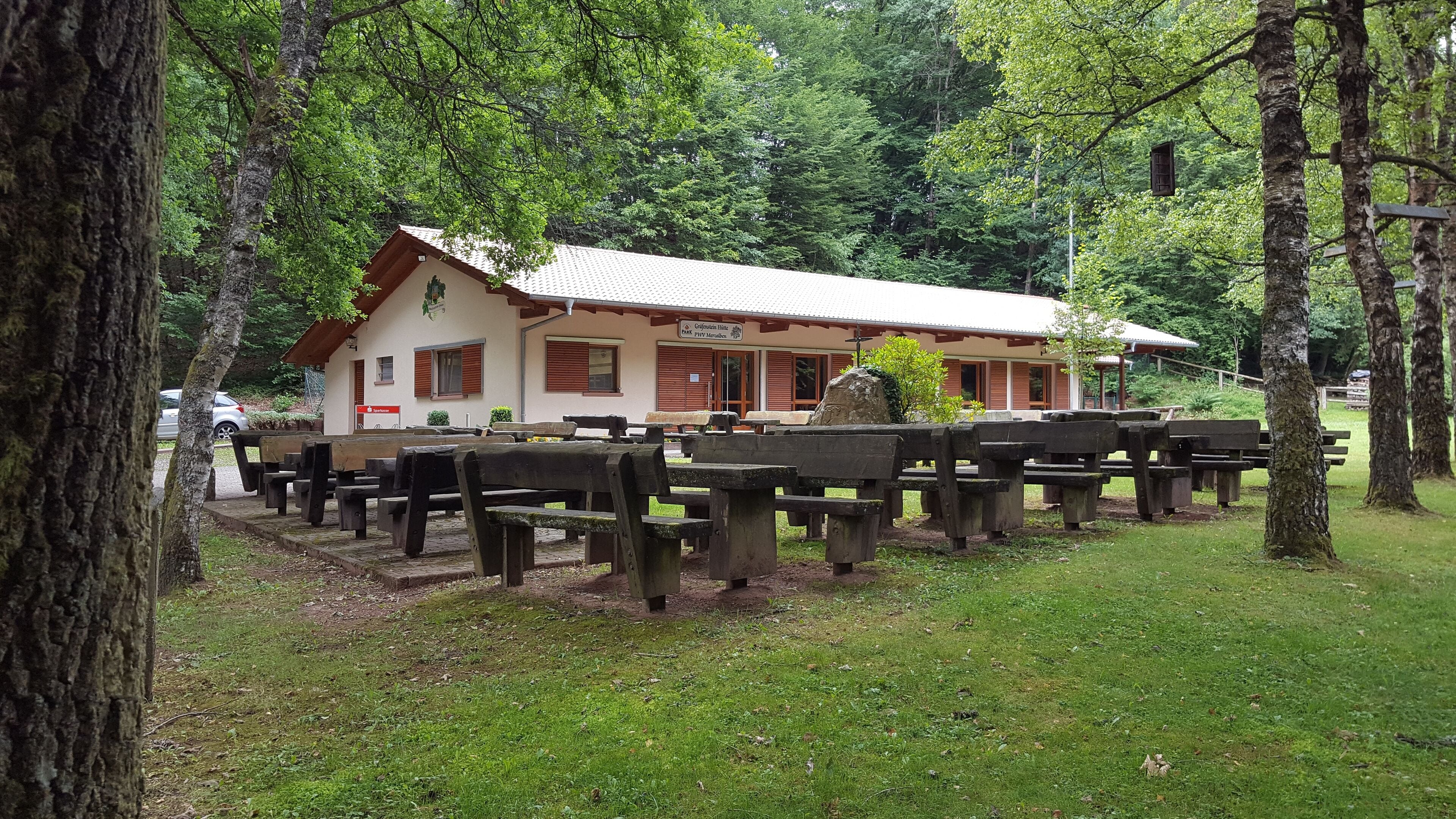A rustic wooden building with picnic tables in a forested area.