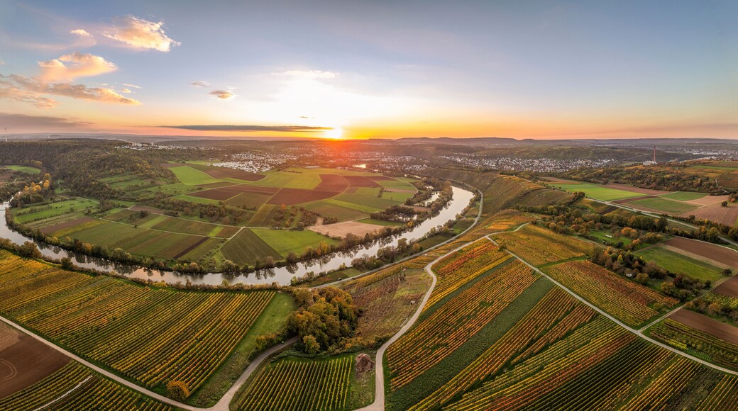 Une rivière serpentant à travers des champs agricoles, avec un coucher de soleil en arrière-plan.