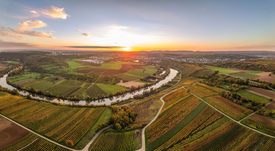 Une rivière serpentant à travers des champs agricoles, avec un coucher de soleil en arrière-plan.