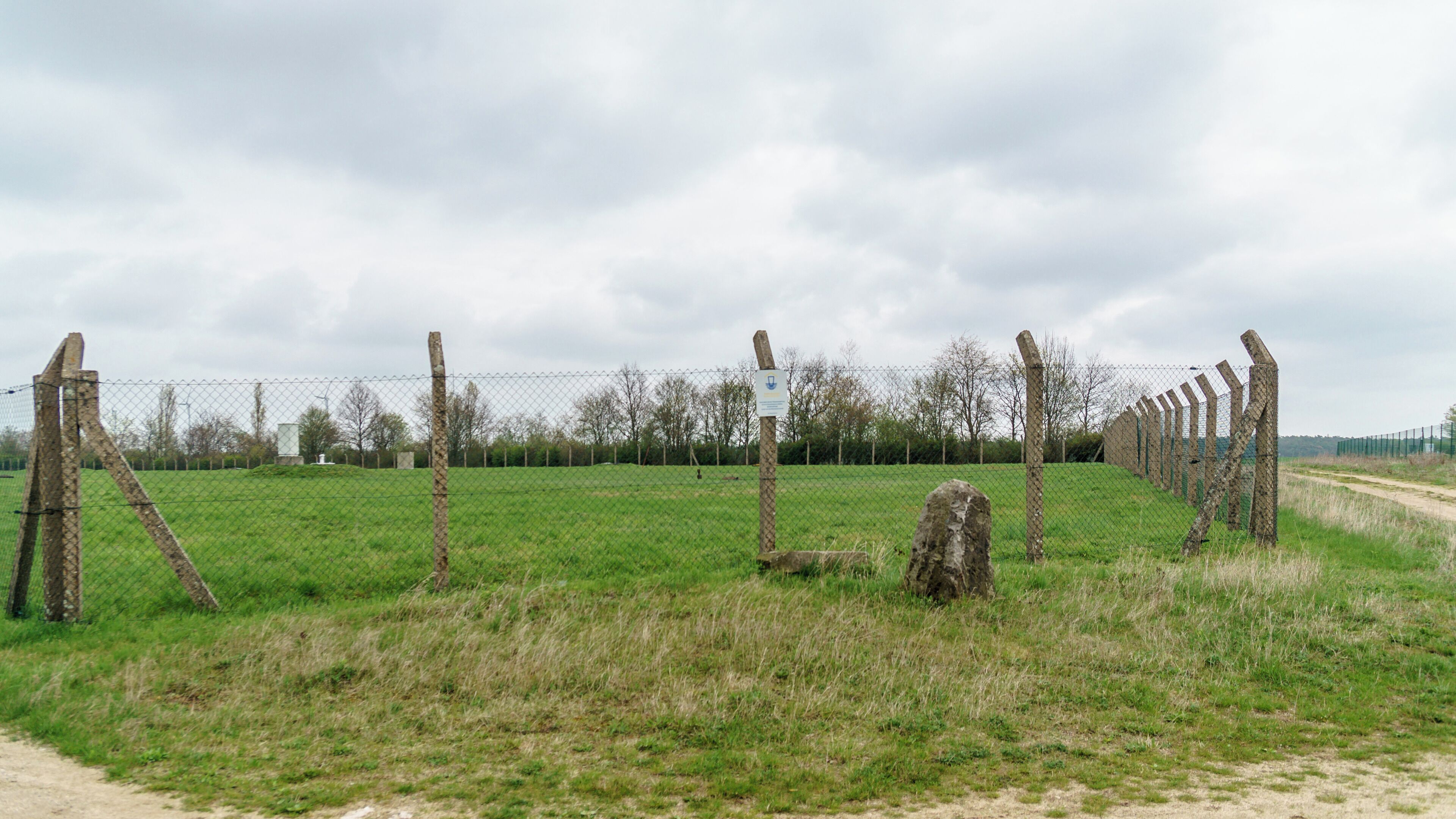 A fenced field with a dirt path, wooden posts, and a sign.