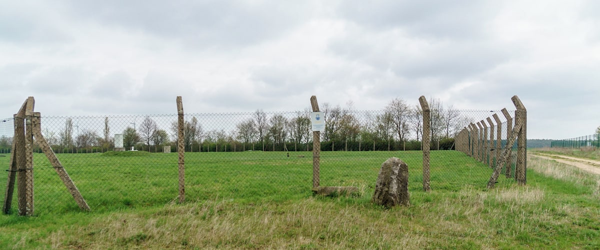 A fenced field with a dirt path, wooden posts, and a sign.