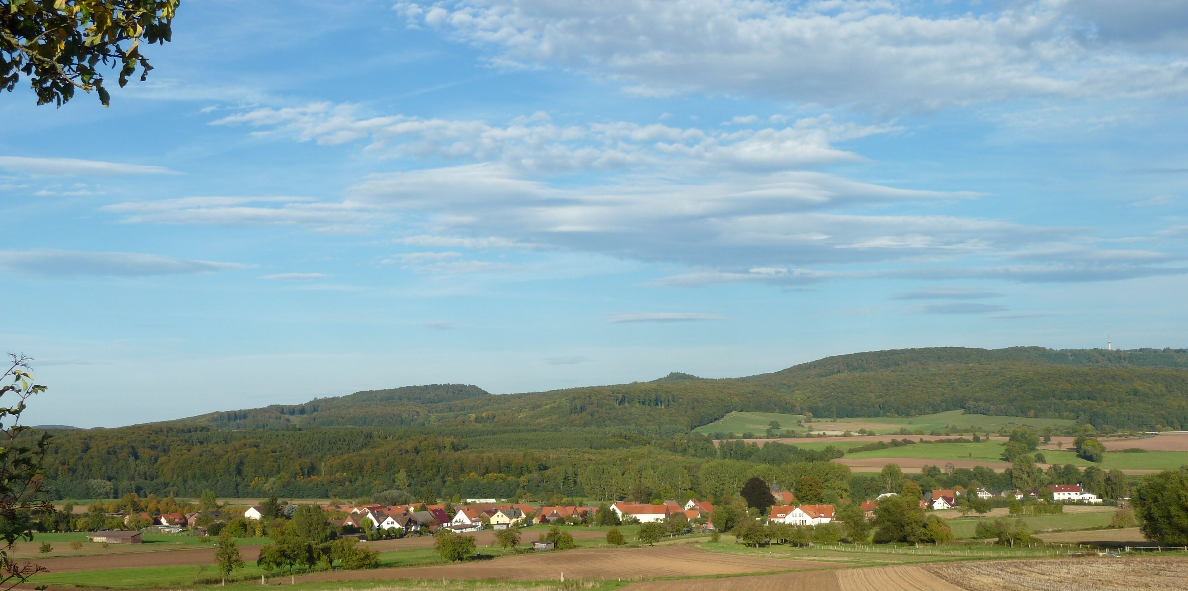 A rural landscape with rolling hills, scattered houses, and a clear sky.