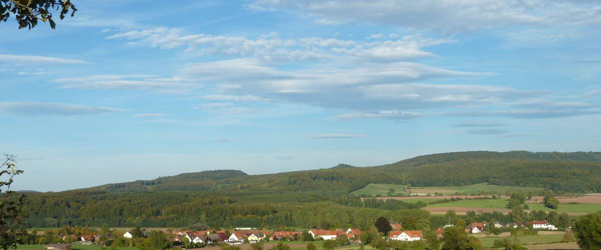 A rural landscape with rolling hills, scattered houses, and a clear sky.