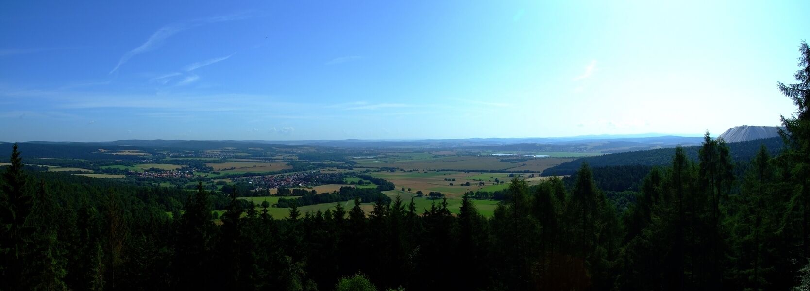 A panoramic view of a valley with a town, forested areas, and distant mountains.