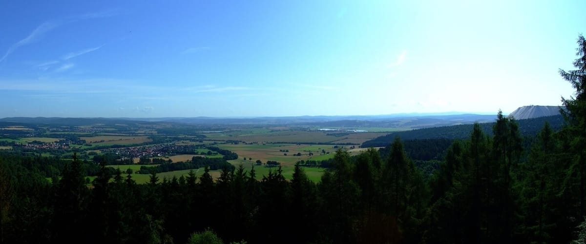 A panoramic view of a valley with a town, forested areas, and distant mountains.