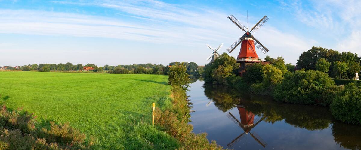 A red windmill, a calm river, and a green field.