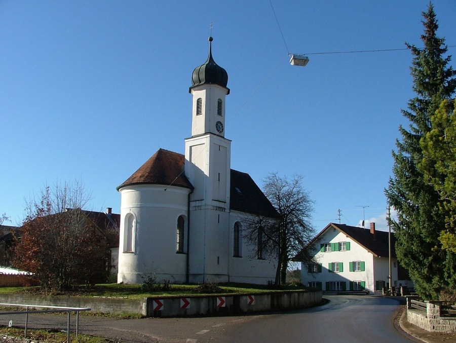 A church with a tall tower and a smaller attached building with green shutters.