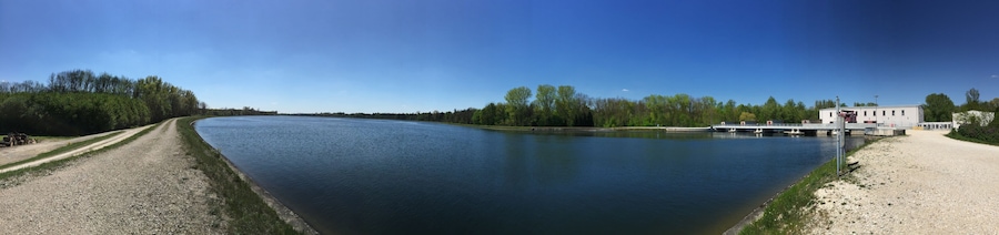 A calm river with a gravel path on the left and a bridge on the right.