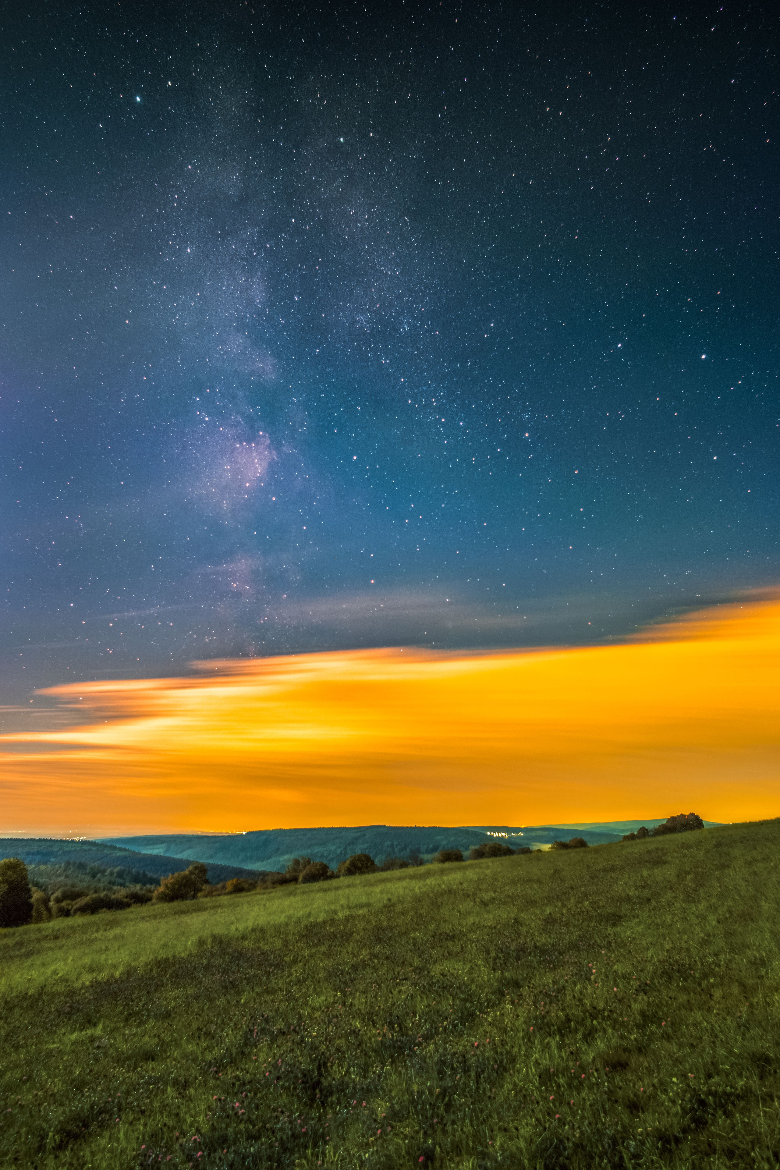 Cielo estrellado sobre un campo de hierba con atardecer.