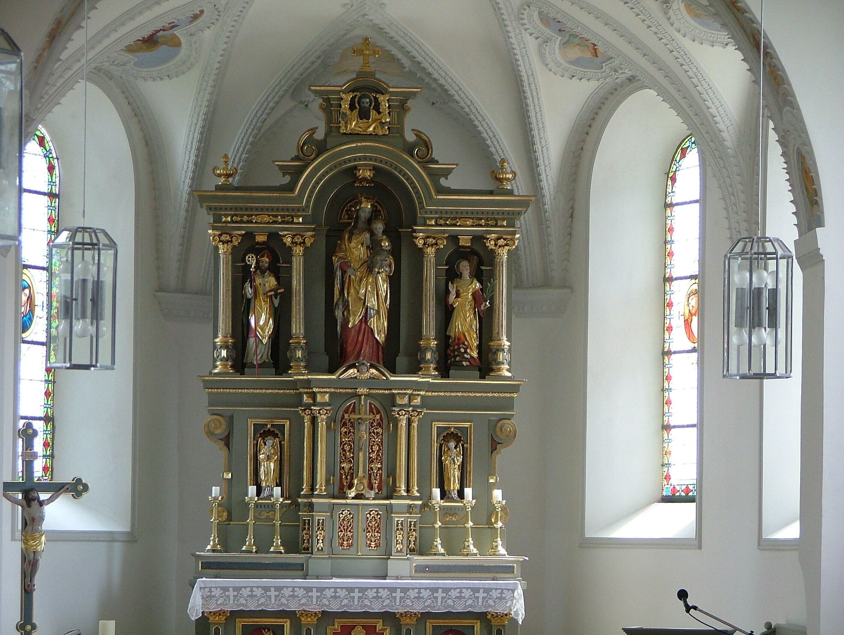 A church interior with a central altar, statues, and stained glass windows.