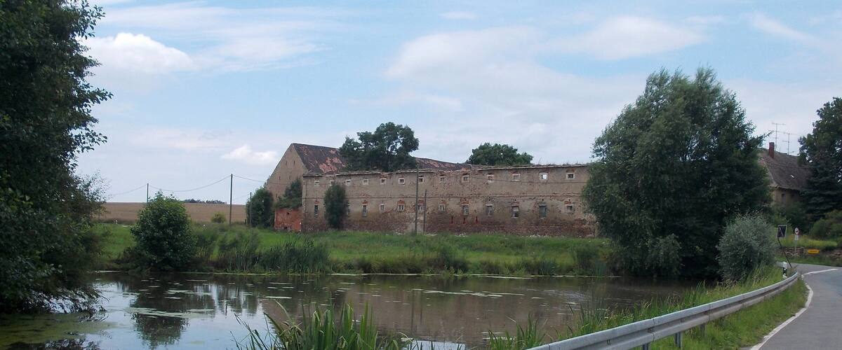 A rural landscape with a river, a dilapidated building, and a guardrail alongside a road.