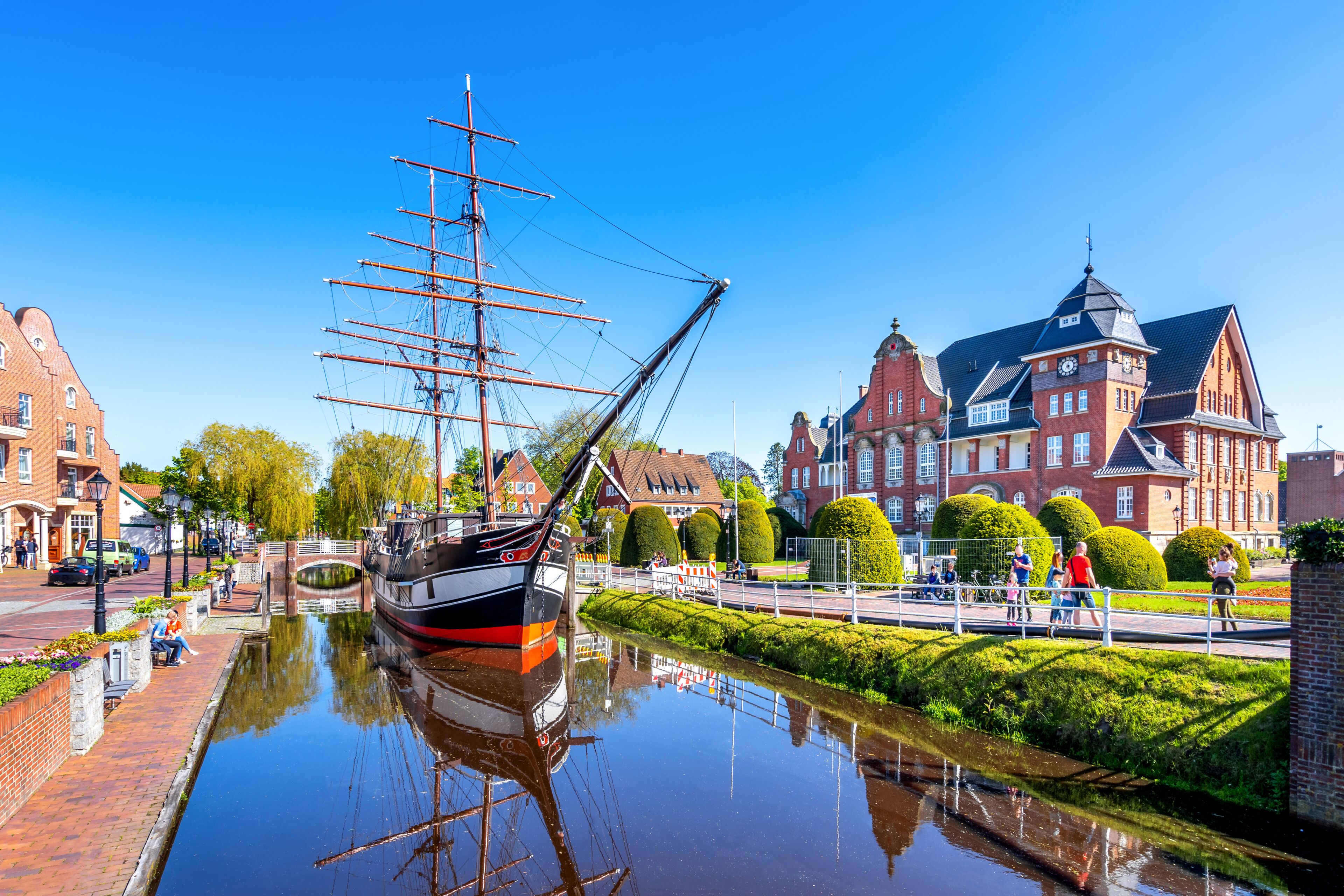 A tall ship docked by a canal, historic buildings, and a clear blue sky.