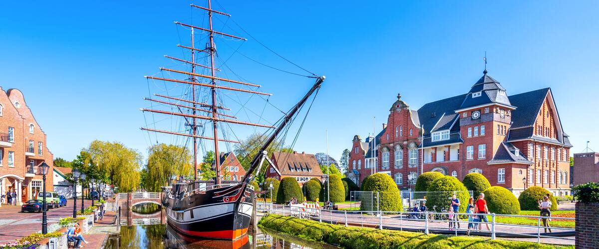 A tall ship docked by a canal, historic buildings, and a clear blue sky.