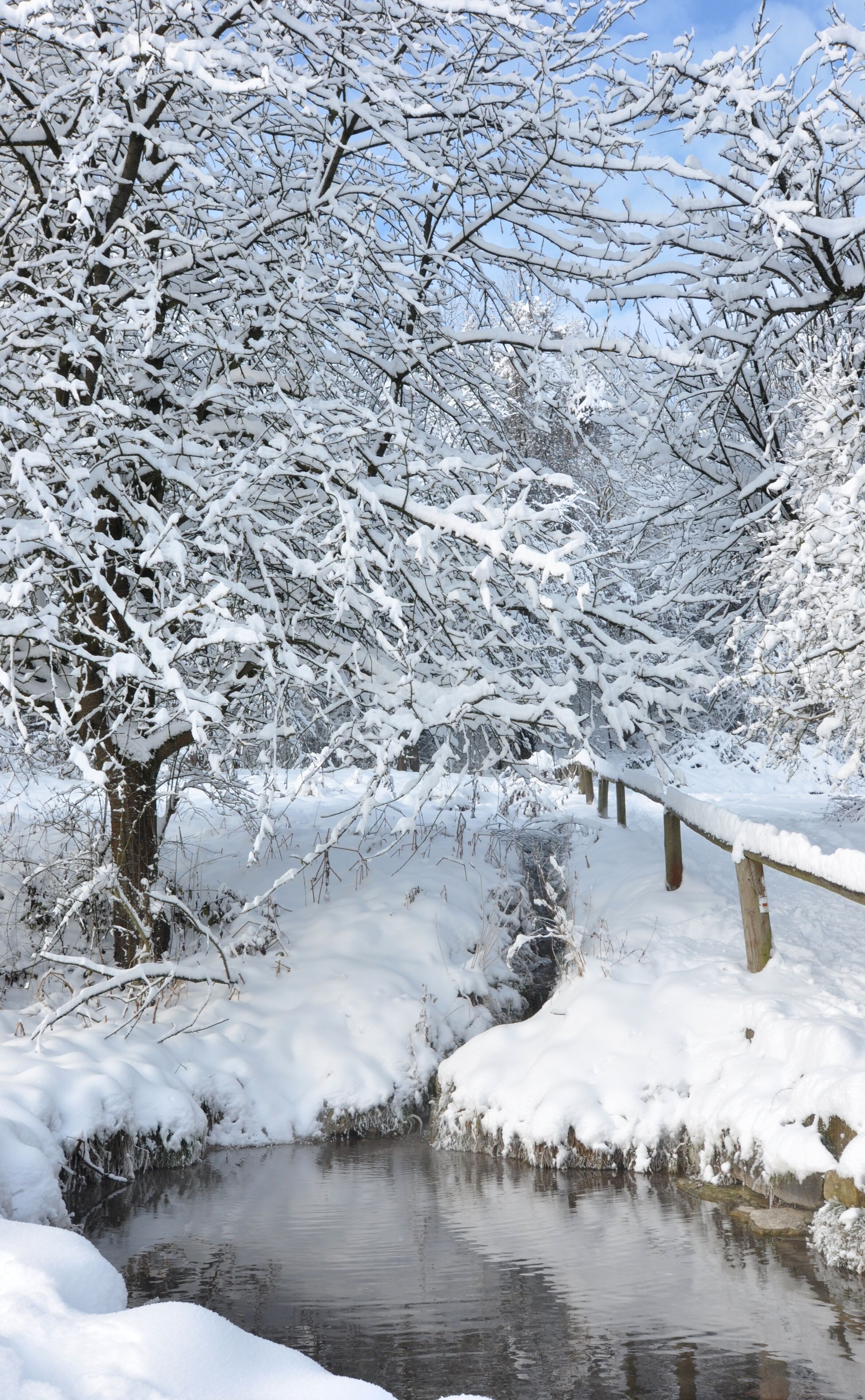 A snow-covered landscape with a wooden bridge over a stream.