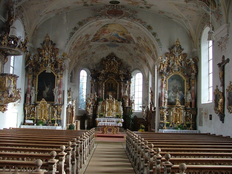 Interior de igreja ornamentado, com tetos altos, frescos detalhados e estátuas douradas.