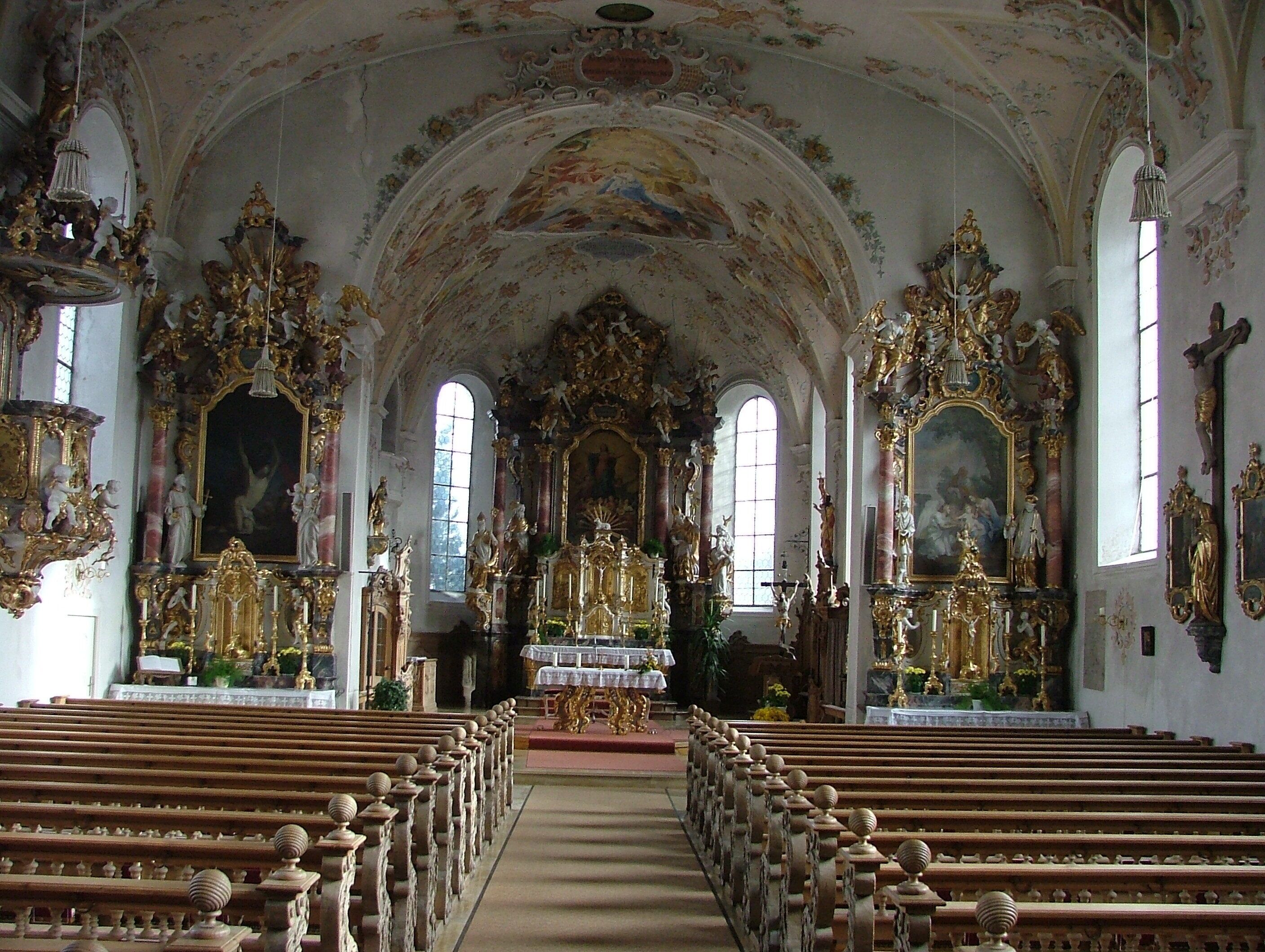 An ornate church interior with high ceilings, detailed frescoes, and golden statues.