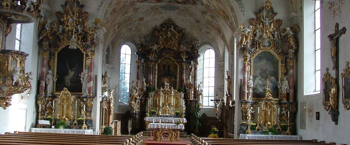 An ornate church interior with high ceilings, detailed frescoes, and golden statues.