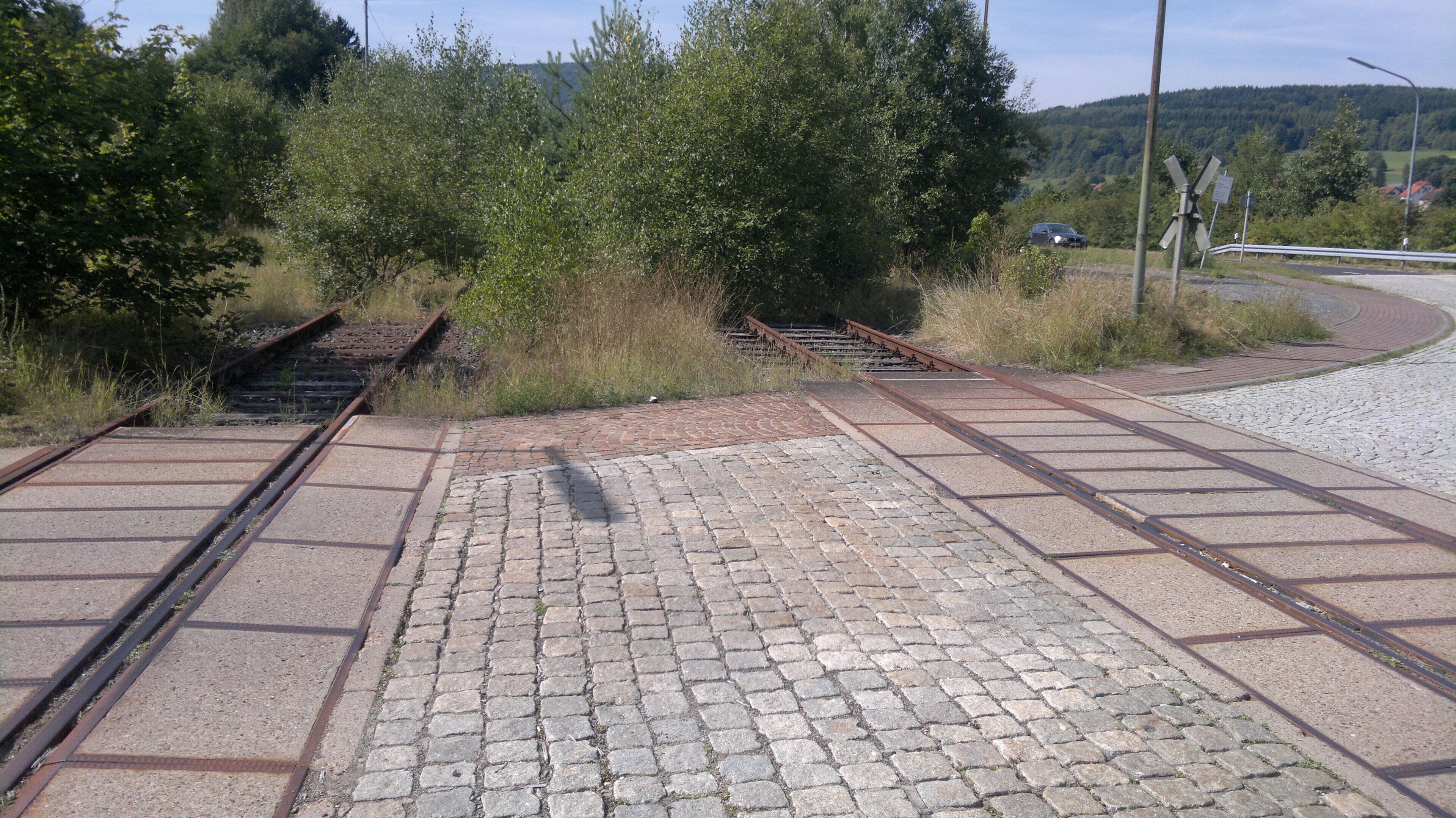 Railway tracks, a paved walkway, and a rural landscape with trees and hills.