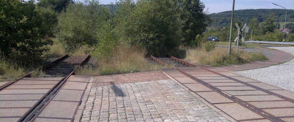 Railway tracks, a paved walkway, and a rural landscape with trees and hills.