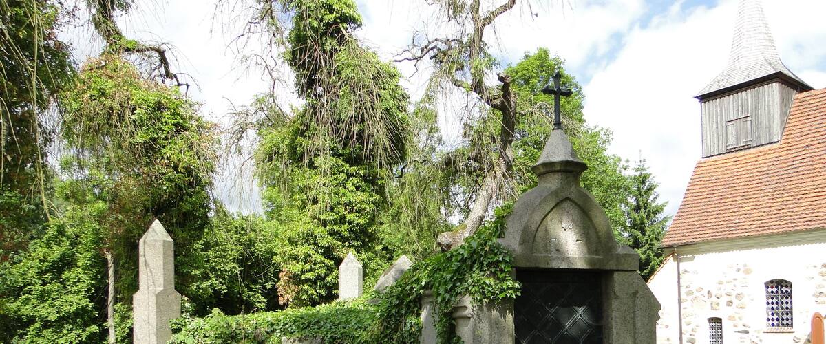 A cemetery with stone crosses, a church, and lush greenery.