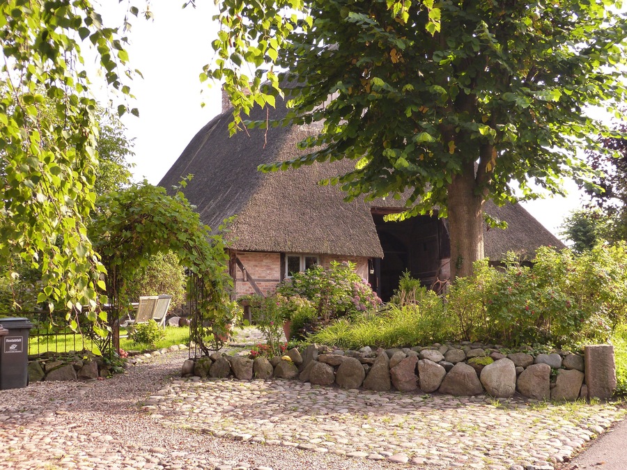 A thatched-roof house surrounded by a stone wall and greenery.