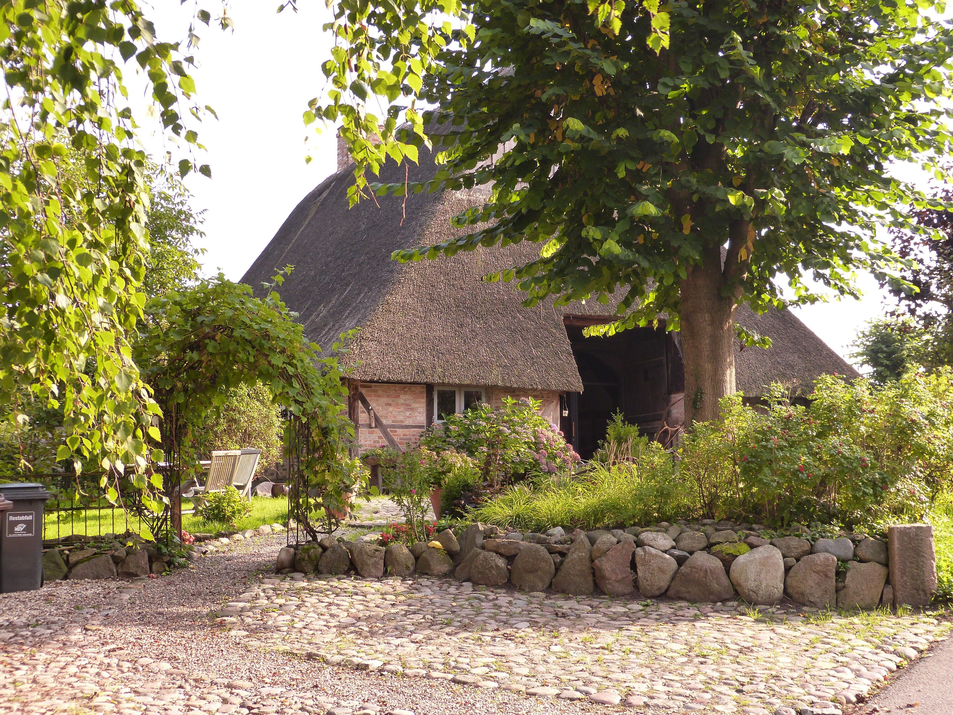 A thatched-roof house surrounded by a stone wall and greenery.