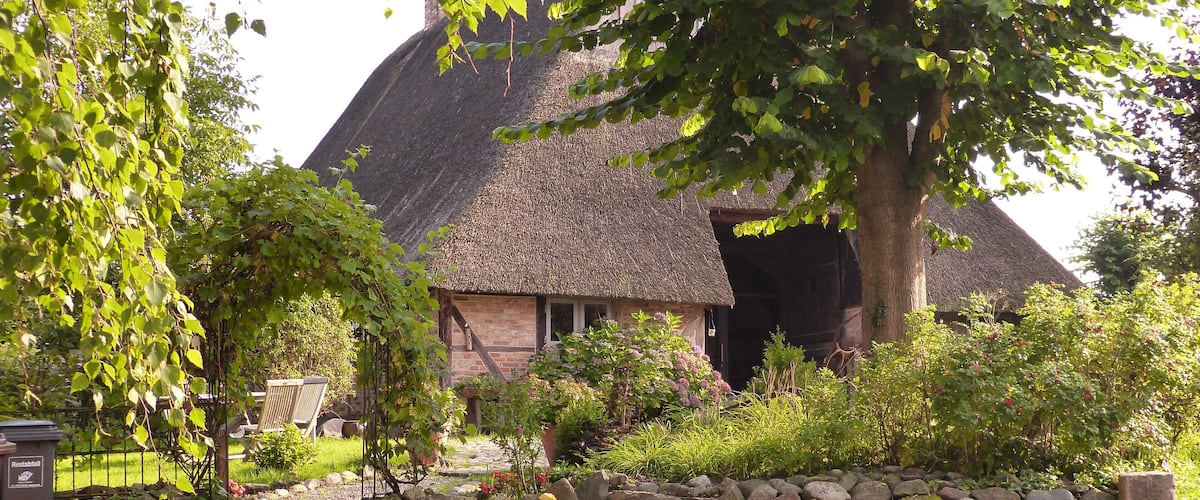 A thatched-roof house surrounded by a stone wall and greenery.