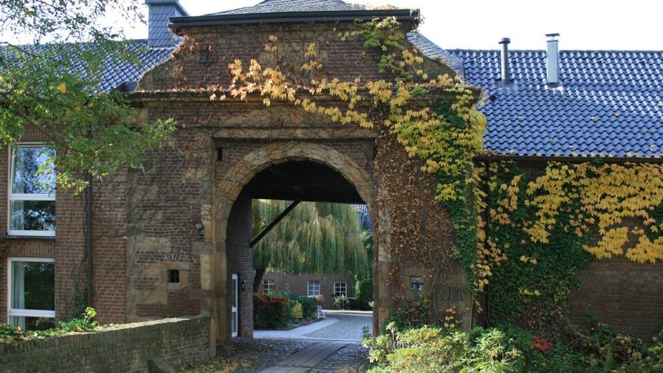 A stone archway with ivy, a cobblestone path, and a building with a tiled roof.