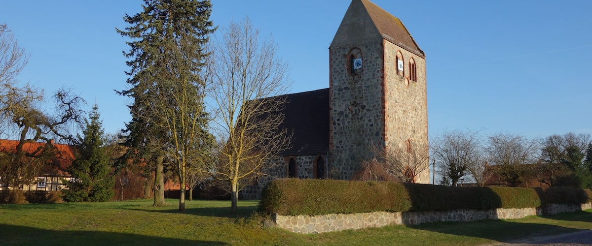 A stone church with a clock tower, surrounded by trees and a cobblestone path.