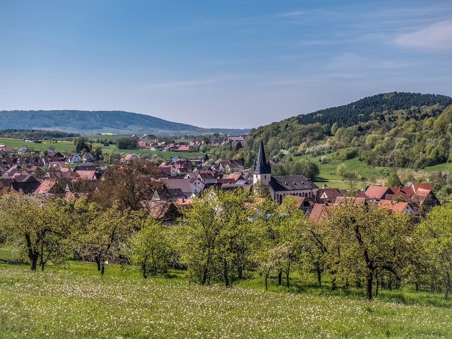 A village with a prominent church, surrounded by lush green hills and blooming trees.