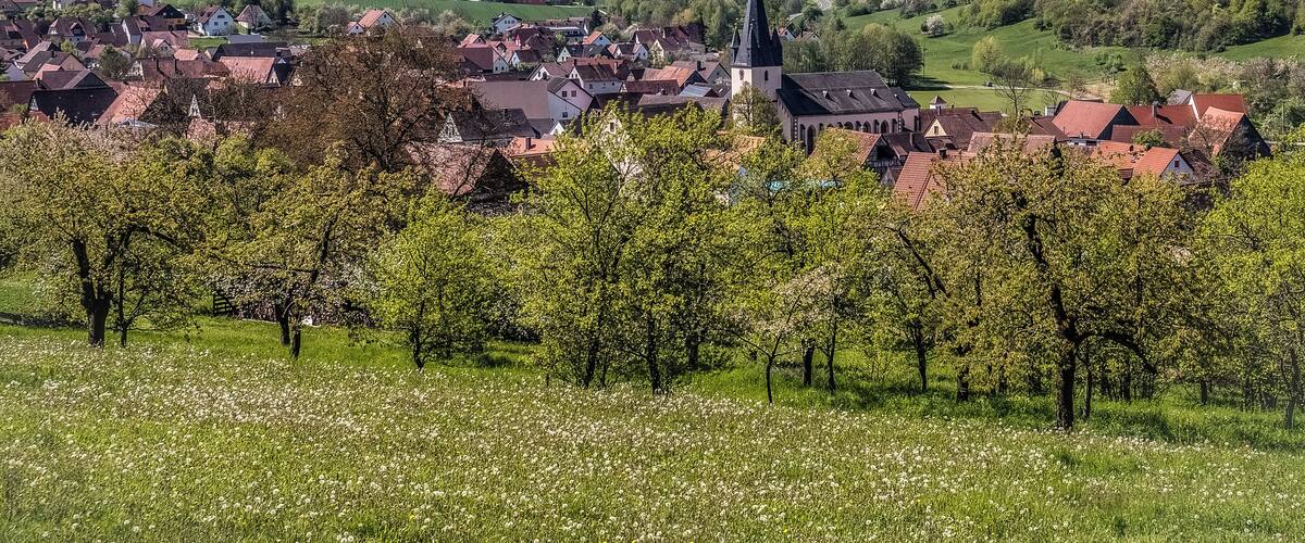 A village with a prominent church, surrounded by lush green hills and blooming trees.