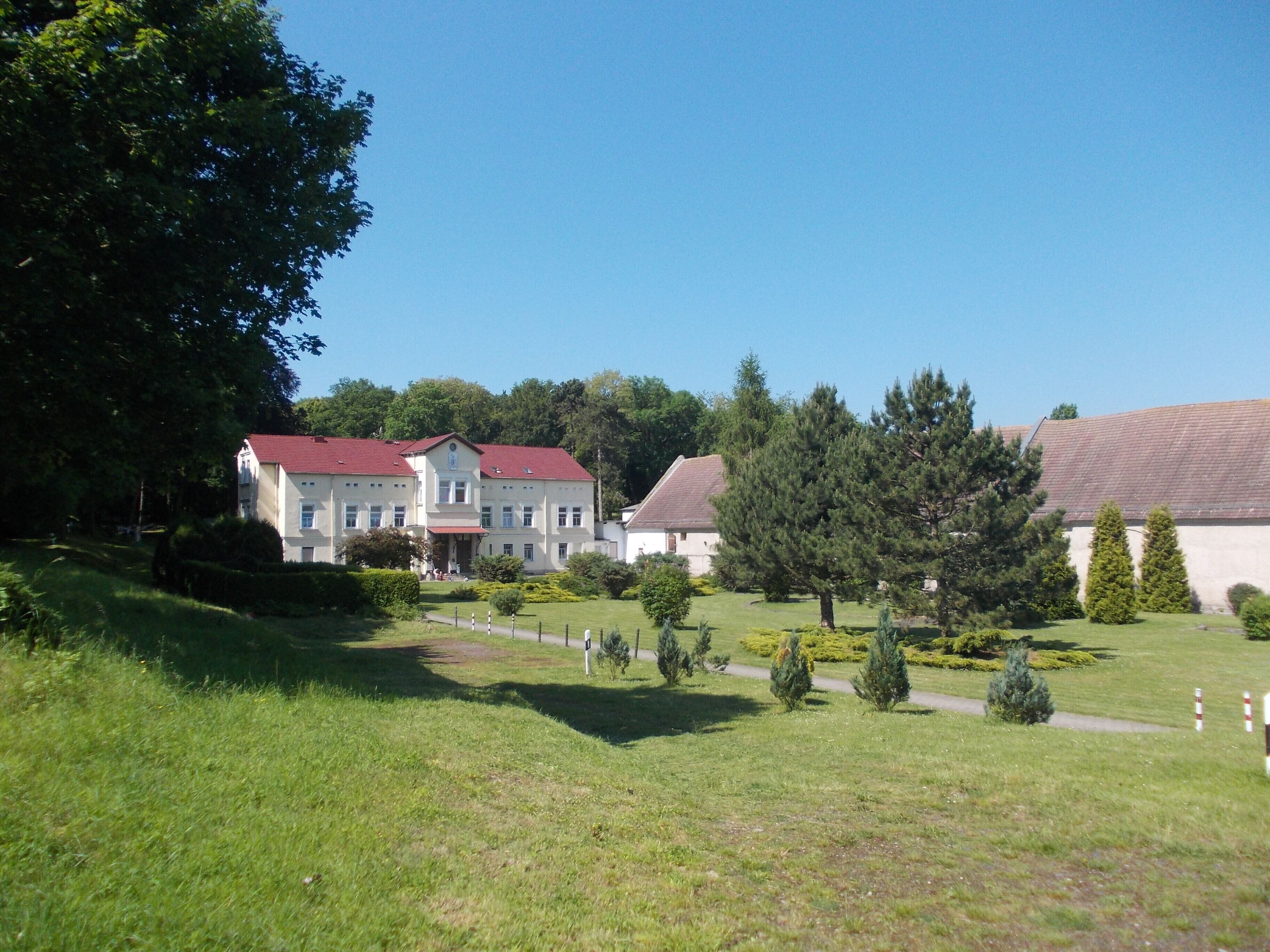 A large building with a red roof, surrounded by green grass and trees.