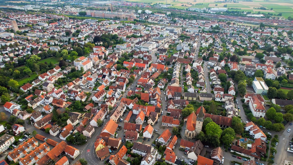 Eine Vogelperspektive auf eine dicht bebautes Städtchen mit roten Dächern, einer Kirche und einem Bahnhof.