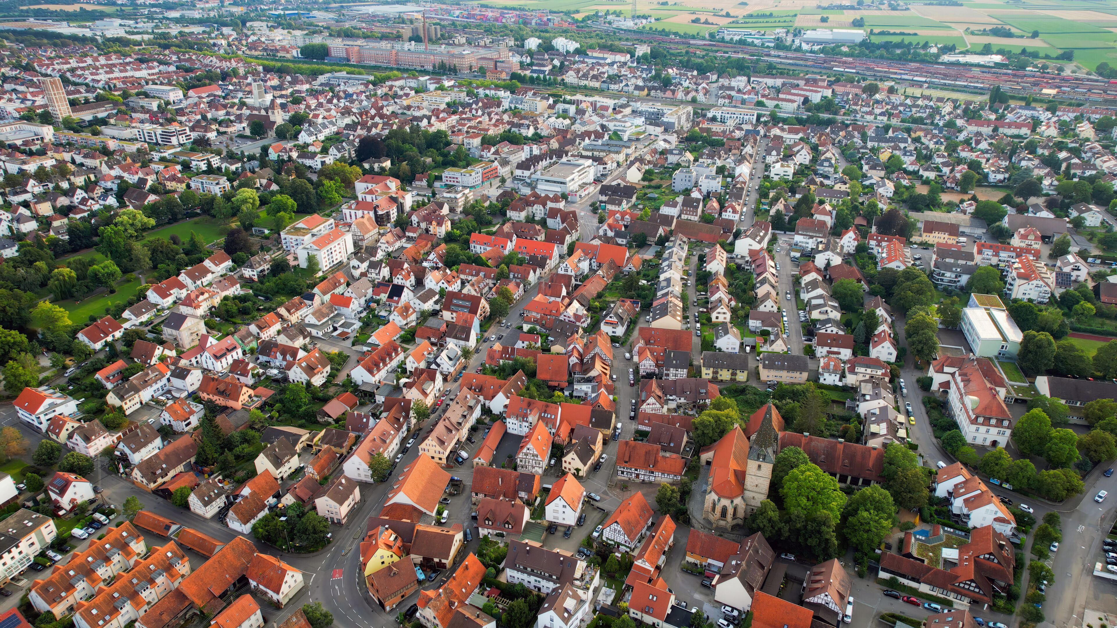 An aerial view of a densely packed town with red-roofed houses, a church, and a train station.