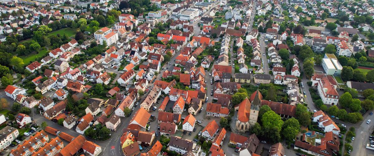 An aerial view of a densely packed town with red-roofed houses, a church, and a train station.