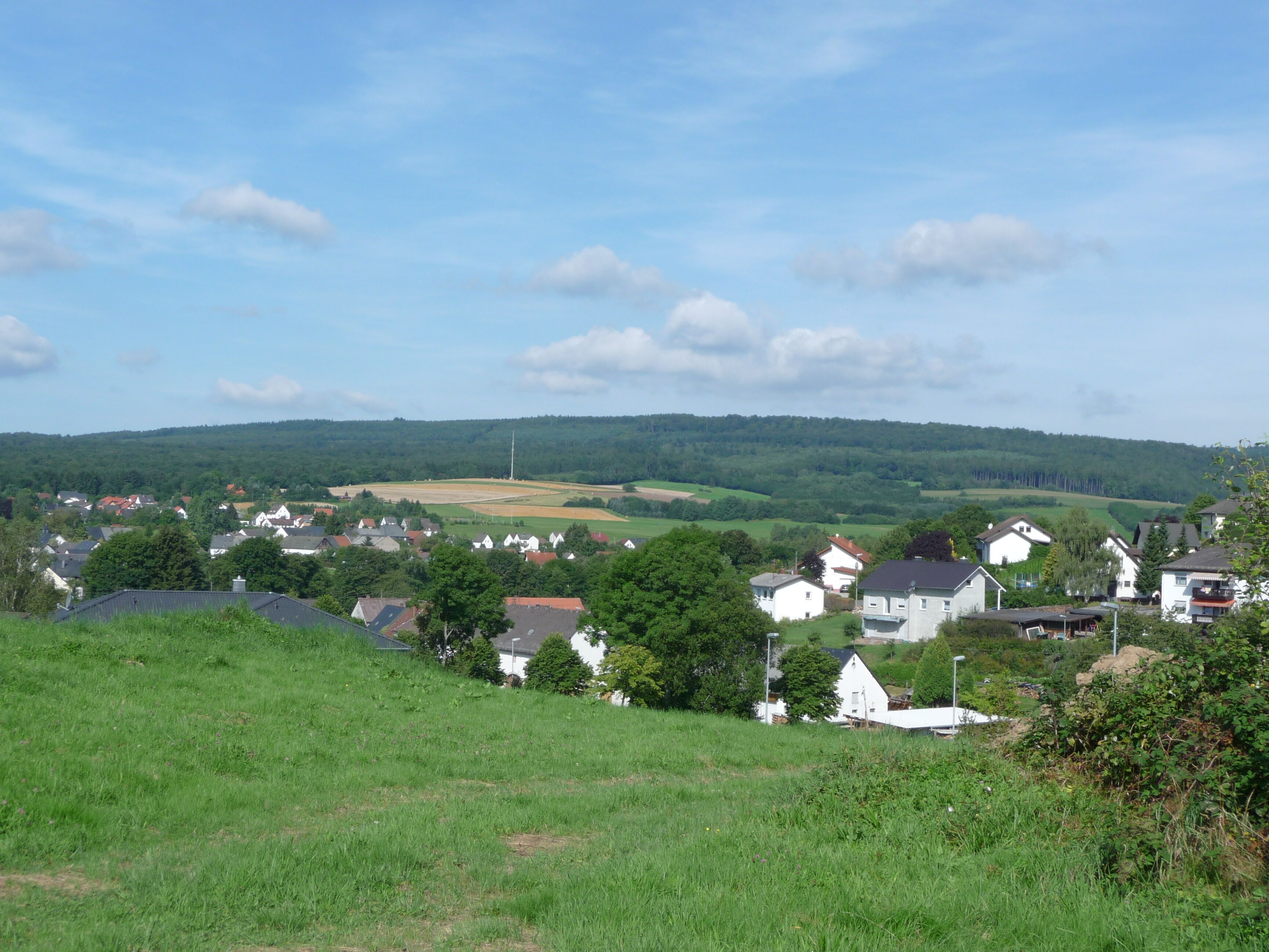 A rural landscape with rolling hills, scattered houses, and a clear sky.