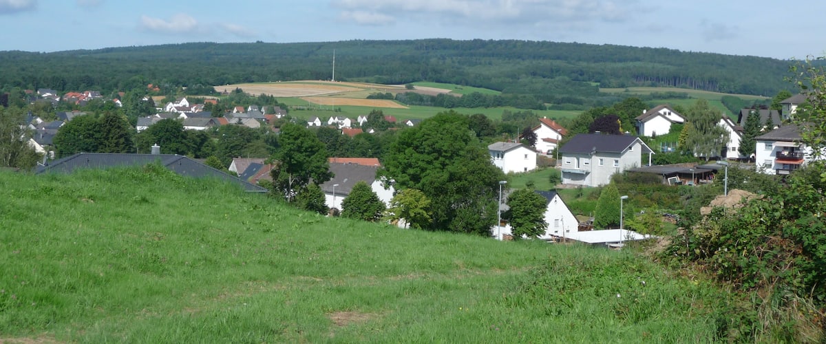 A rural landscape with rolling hills, scattered houses, and a clear sky.