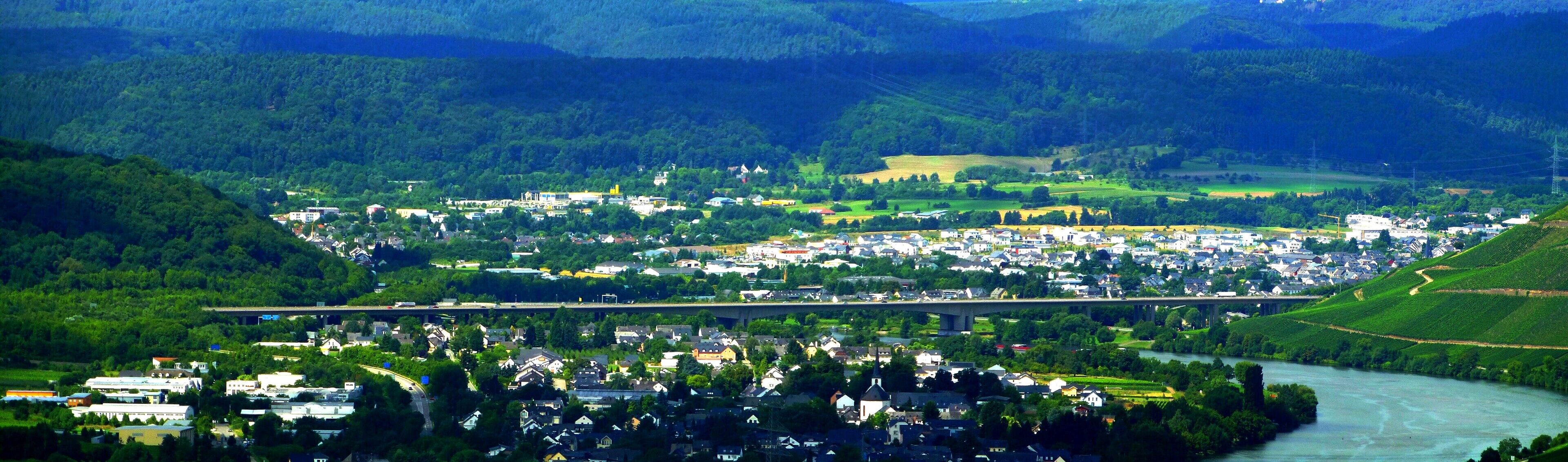 A river flowing through a town surrounded by hills and greenery.