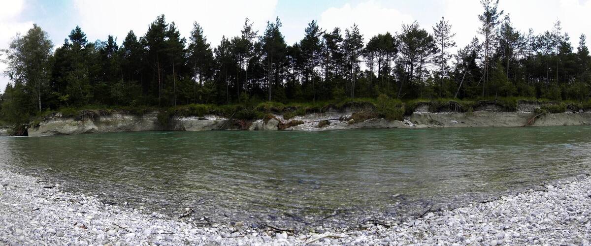 A river with clear water, surrounded by a rocky shoreline and dense forest.