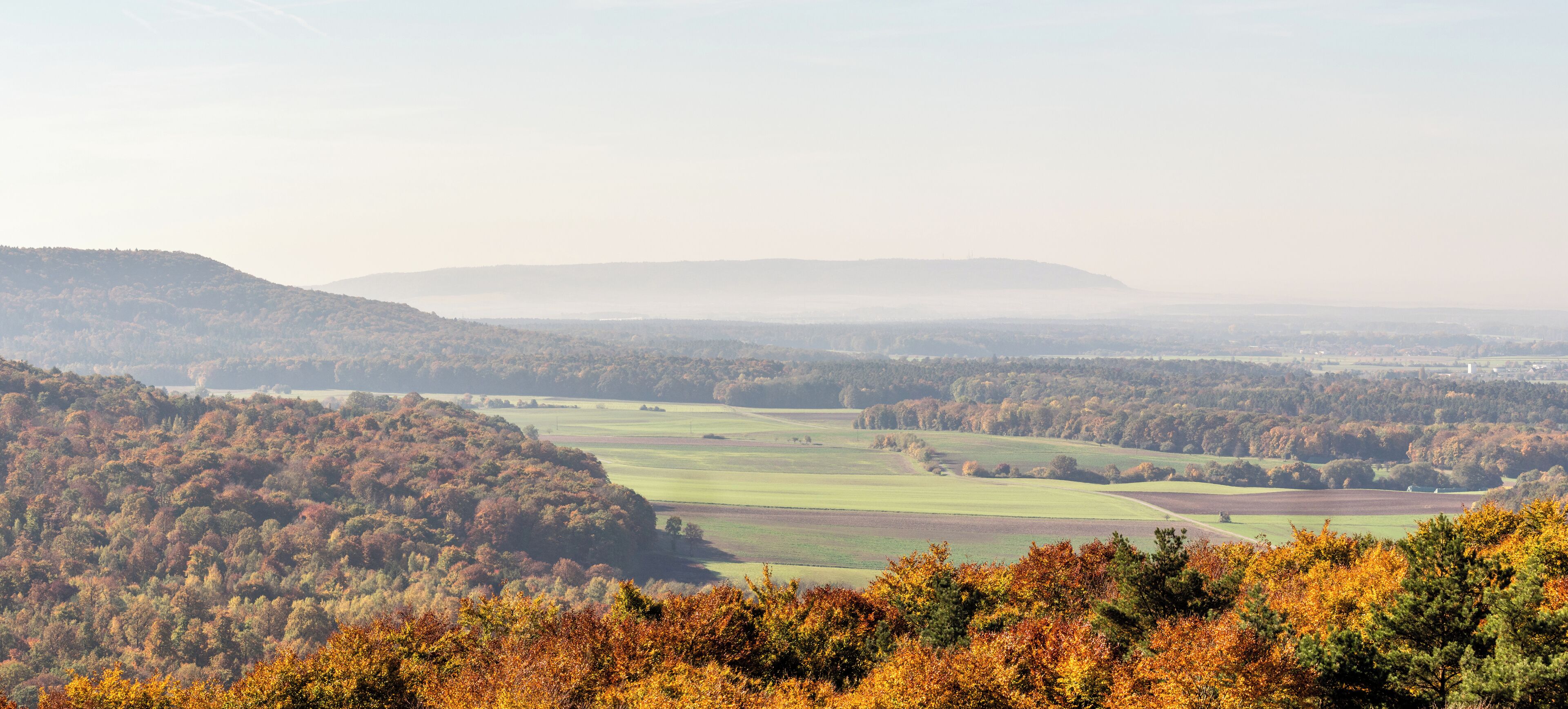 A valley with autumn foliage, rolling hills, and distant mountains.
