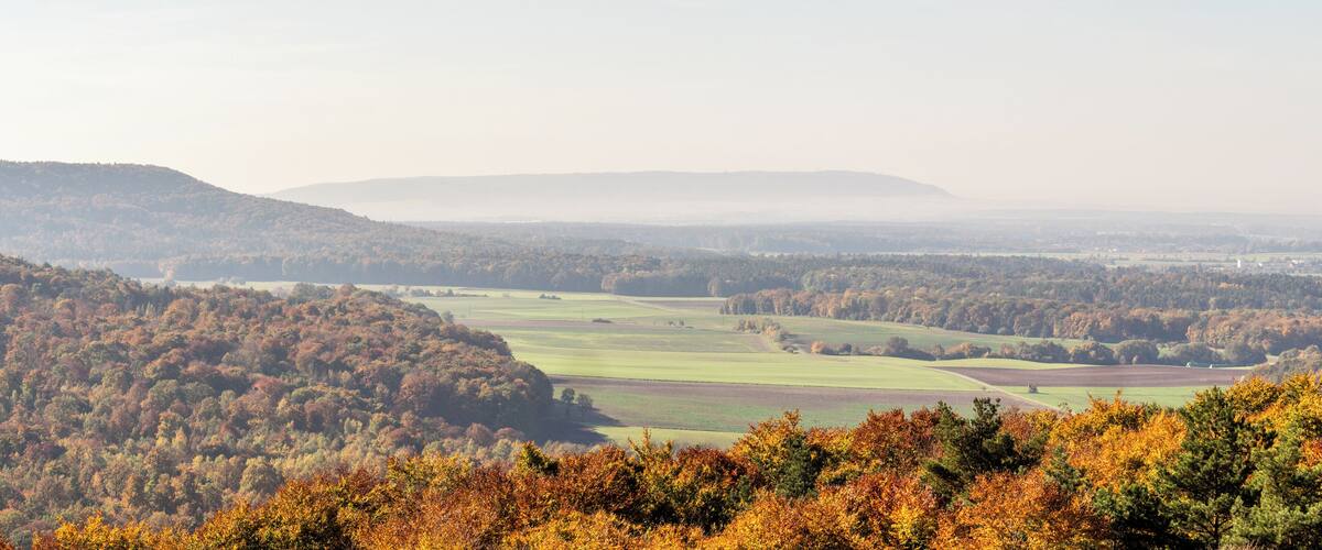 A valley with autumn foliage, rolling hills, and distant mountains.