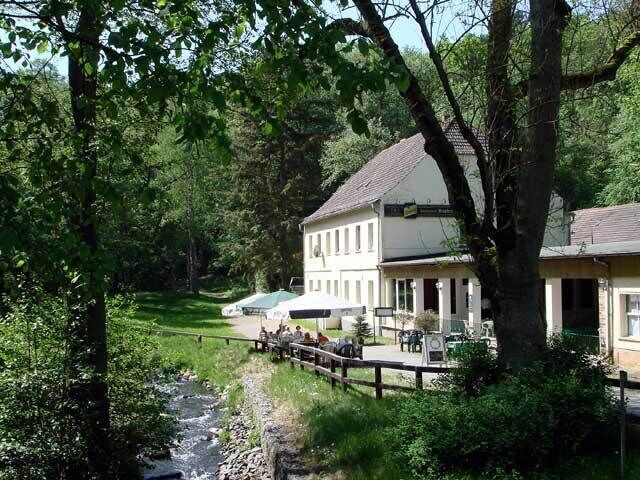 A riverside building with a wooden deck, surrounded by lush greenery and trees.