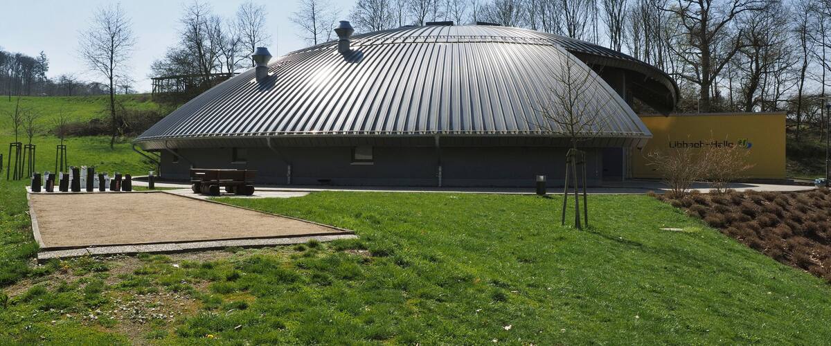 A modern building with a curved roof, surrounded by a grassy area and trees.