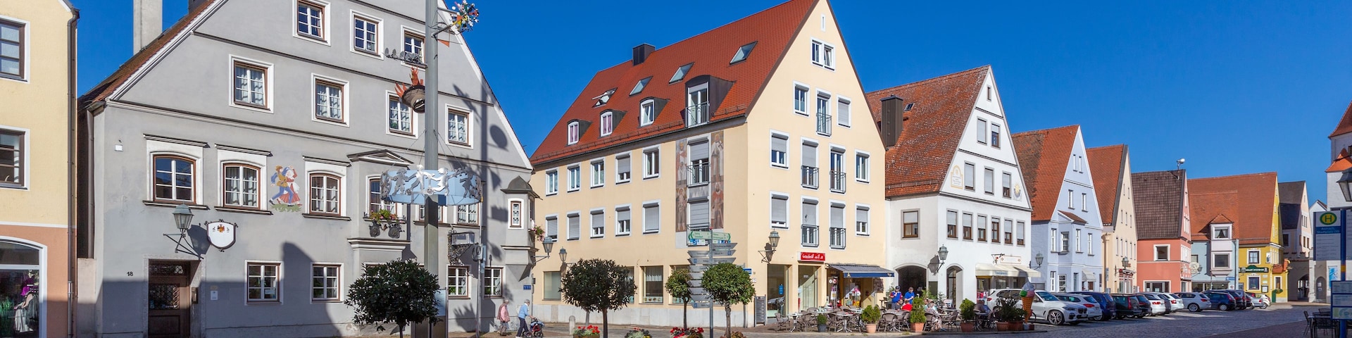 Eine Kopfsteinpflasterstraße gesäumt von traditionellen europäischen Gebäuden, ein klarer blauer Himmel und einige Fußgänger.